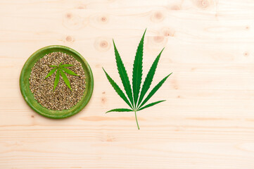 Green cannabis leaf and seeds on yellow plate on wooden background. Vegetarian food concept