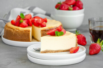 Homemade cheesecake New York with fresh strawberries on a white plate with coffee on a gray stone background. American cuisine.