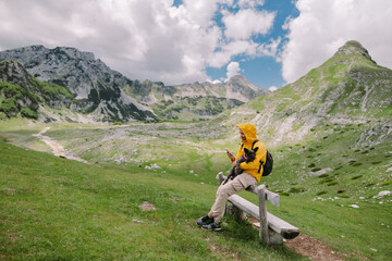 man travel with dog using smartphone at countryside with mountains scenic view. Backpacker man...