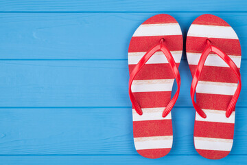 Top above overhead view close-up photo of a pair of striped flipflops placed to the right side isolated on blue wooden background with copyspace