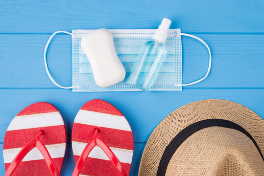 Vacation and quarantine concept. Top above overhead view photo of soap sanitizer mask flipflops and hat isolated on blue background