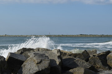 Waves crash against rock on the Atlantic Ocean. A lighthouse stands in the distance.