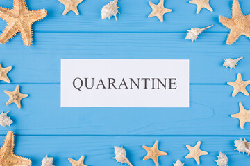 Summer in quarantine concept. Top above overhead view photo of quarantine word and seashells and seafish isolated on blue wooden background