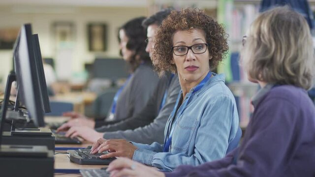 Line of mature multi-cultural students sitting at computers in library learning IT skills and helping each other - shot in slow motion