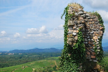 
hilly panorama of vineyards with mountains in the background and blue sky with incoming clouds with ruins of a brick wall in the foreground
