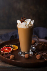 A glass of coffee latte with cakes and truffles on a dark background.