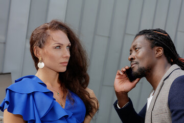 African man and European Caucasian woman on a walk in the city, man talking on the phone. Summer day