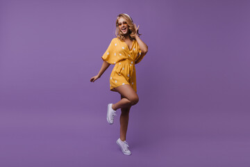 Full-length portrait of jumping happy woman in summer outfit. Studio shot of attractive european girl expressing happiness on purple background.