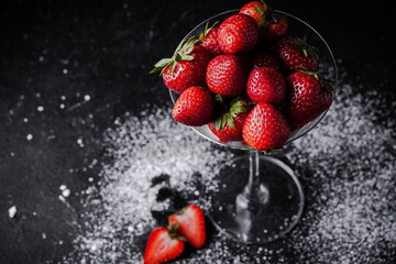 Close up shot of the martini cocktail glass filled with strawberries and sprinkled with a powdered sugar on the black background