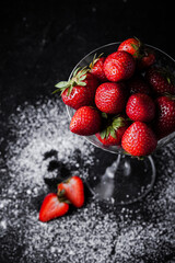 Close up shot of the martini cocktail glass filled with strawberries and sprinkled with a powdered sugar on the black background