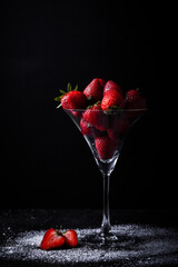 Close up shot of the martini cocktail glass filled with strawberries and sprinkled with a powdered sugar on the black background