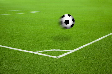 Football in motion on soccer court with white stripes corner markings. Saturated green grass and football in the air with motion blur and cast shadow.