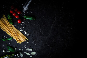 Long spaghetti with cherry tomatoes, sea salt garlic and olive oil on the black concrete table. Overhead shot of Italian pasta with ingredients on the dark background