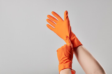 caucasian male person putting on orange washing gloves. washing and cleaning service concept. minimal. copy space. grey background. studio shot.