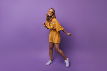 Blissful shapely girl in orange glasses posing on purple background. Indoor photo of laughing cheerful woman expressing happiness.