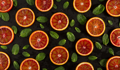 Round slices of citrus, red mandarin with green mint leaves on a black background. Top view is randomly arranged as a background texture. The idea of conception.
