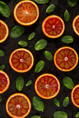 Round slices of citrus, red mandarin with green mint leaves on a black background. Top view is randomly arranged as a background texture. The idea of conception.