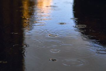 Drops of rain bubbling in a puddle with the reflection of light