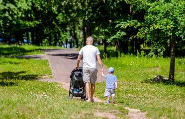 Father with her son and a baby stroller walking in the summer Park
