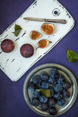 Fresh plum and figs on a cutting white board and purple background.