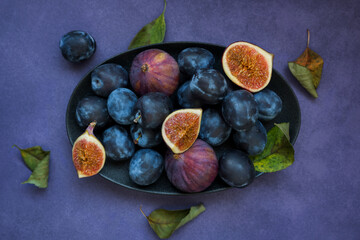 Ripe plums and figs on a black dish and purple background. Beautiful food photo