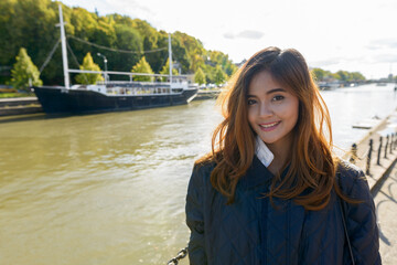 Fototapeta premium Young happy Asian woman standing in pier with vintage black boat in the river