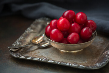 Red plums in a bowl on a silver tray old. Still life in retro style.