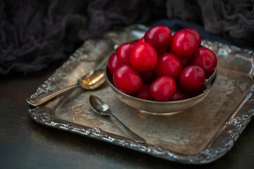 Red plums in a bowl on a silver tray old. Still life in retro style.