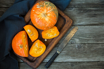 Ripe orange pumpkin is cut on a board, on an old wooden background, a table