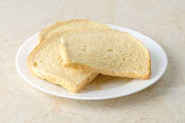 Few slices of wheat bread dried enough to make bread crumbs on a white plate over a kitchen table. Ingredient for meatballs and cutlets. Cook at home.