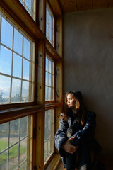 Fototapeta premium Young beautiful Asian woman sitting in front of closed wooden window with sunlight streaming in