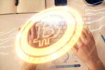 Double exposure of man's hands typing over computer keyboard and crypto currency theme hologram...