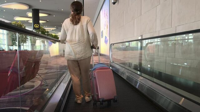 woman with luggage is on moving walkway