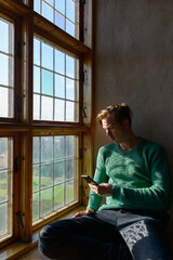 Young handsome man using mobile phone in front of closed wooden window