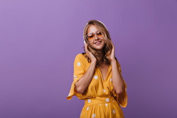 Debonair female model in summer attire enjoying music. Enthusiastic white lady expressing positive emotions on purple background.