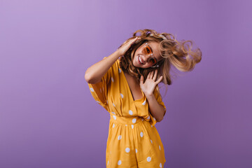 Beautiful active girl posing on purple background. Studio shot of carefree blonde lady dancing with smile.