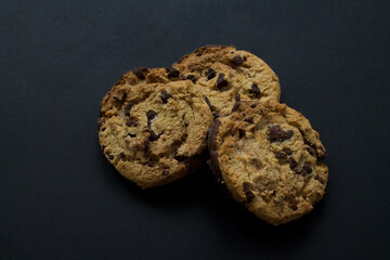 Three delicious chocolate chip cookies on black background.