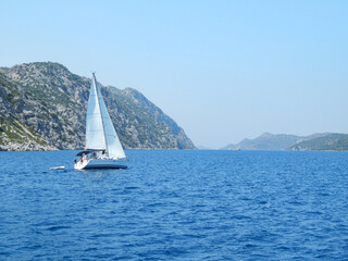 Fototapeta premium Small white yacht floats near the rocky shores, sea, rocks