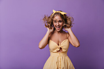 Stunning woman with bronze skin jumping on purple background. Indoor photo of cute smiling girl with blonde curly hair.