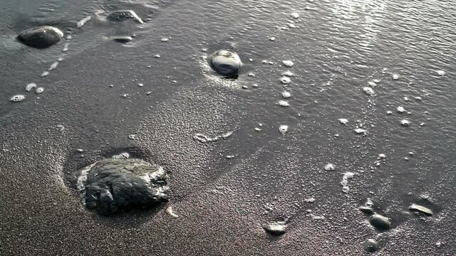 Sea waves run against black stones and dark sand.