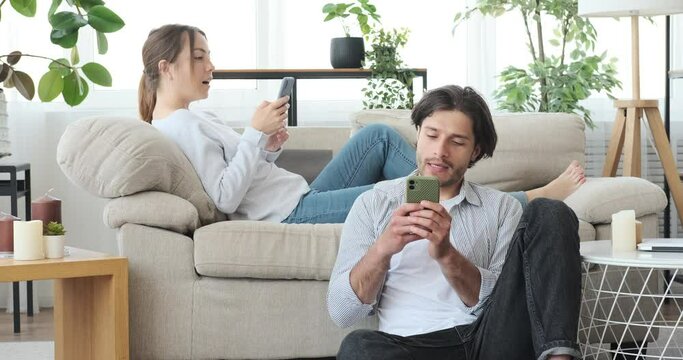 Millennial couple busy text messaging using mobile phone at home