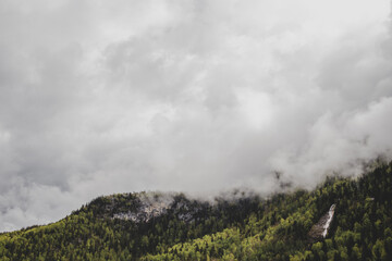 Konigsbach waterfall on background of mountains covered by dense forest & grey clouds. Bavaria. Germany