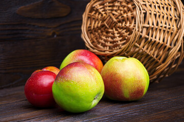 Apples and plums on a brown wooden background. Fresh fruits. Harvest. Healthy food. A wicker basket. Stick basket