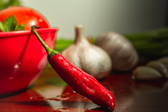 Close up em pimenta do dedo da mo&ccedil;a e composi&ccedil;&atilde;o de fundo desfocado com alho, tomate e vegetais. Pimenta fresca com gotas de &aacute;gua