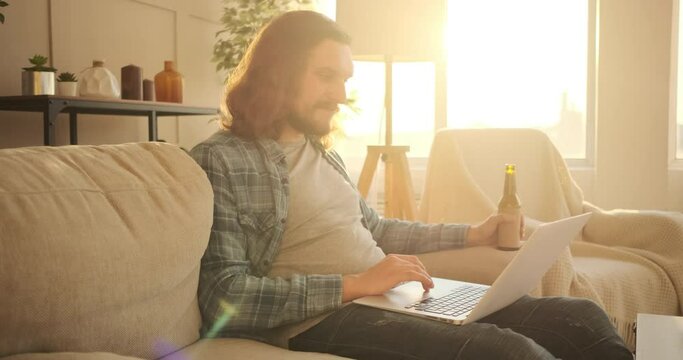 Handsome man using laptop and drinking beer at home