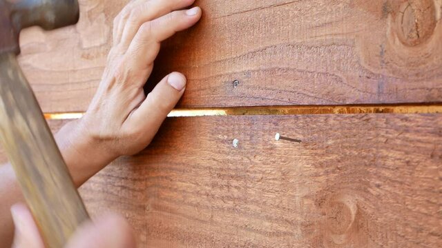 Close up of man's hands hammering a nail into a wooden wall