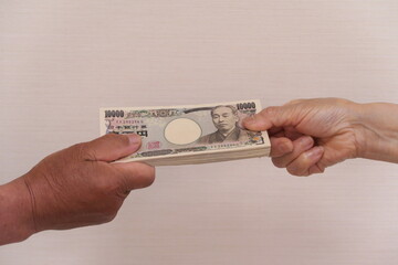 持続化給付金の100万円を渡す手と受け取る手。男性と女性の手。1万円札100枚。
