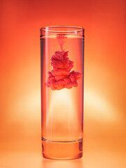 Ink cloud in glass of water. Mixing paint in water on red background. Monochrome color theme