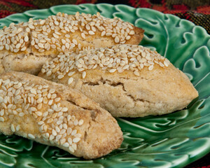 Sticks of chorek (Armenian sweet bread) with sesame seeds on green ceramic dish sitting on homemade lace table rummer. 