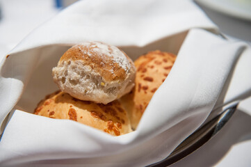 Fresh white cloth napkin encases out-of-the-oven dinner rolls on restaurant table. 